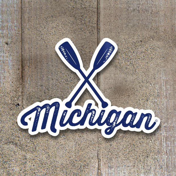 Sticker with crossed paddles and 'Michigan' text on a wooden background